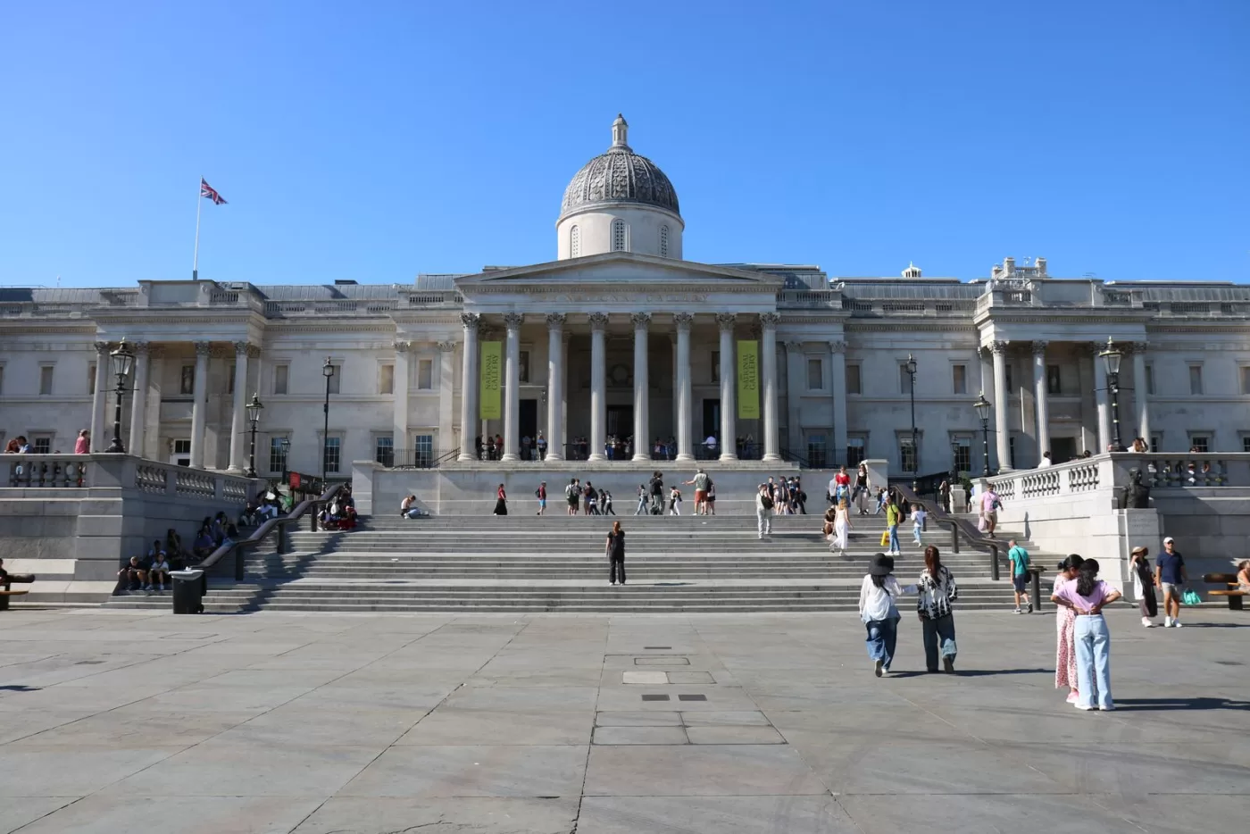 The National Gallery in Trafalgar Square, London, with people enjoying a sunny day.