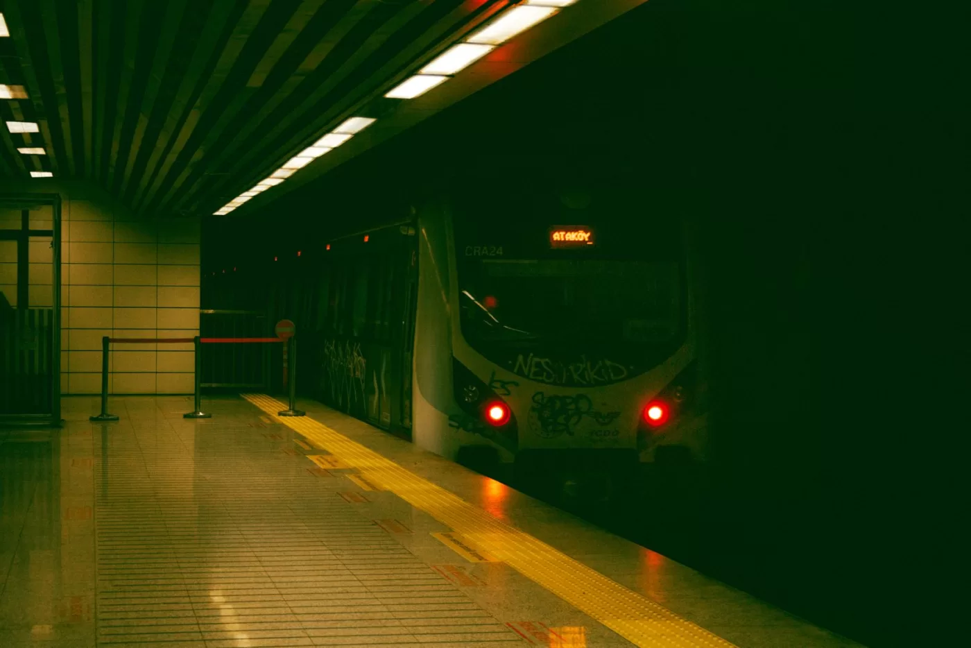 A graffiti-covered subway train approaches an empty underground platform with yellow safety markings.
