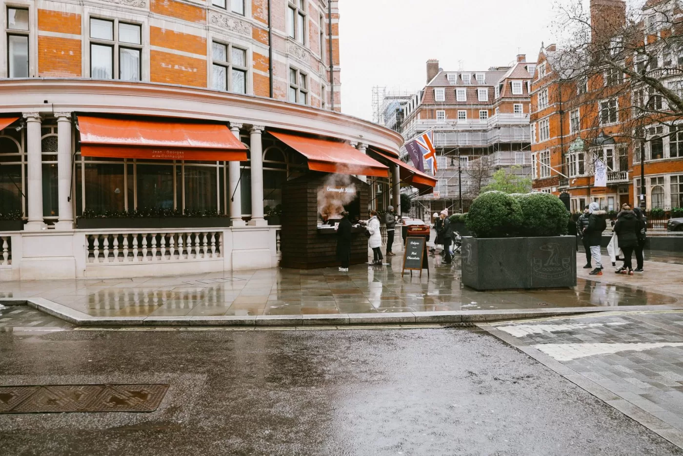 A street scene in London with people, wet pavement, and iconic architecture on a rainy day.