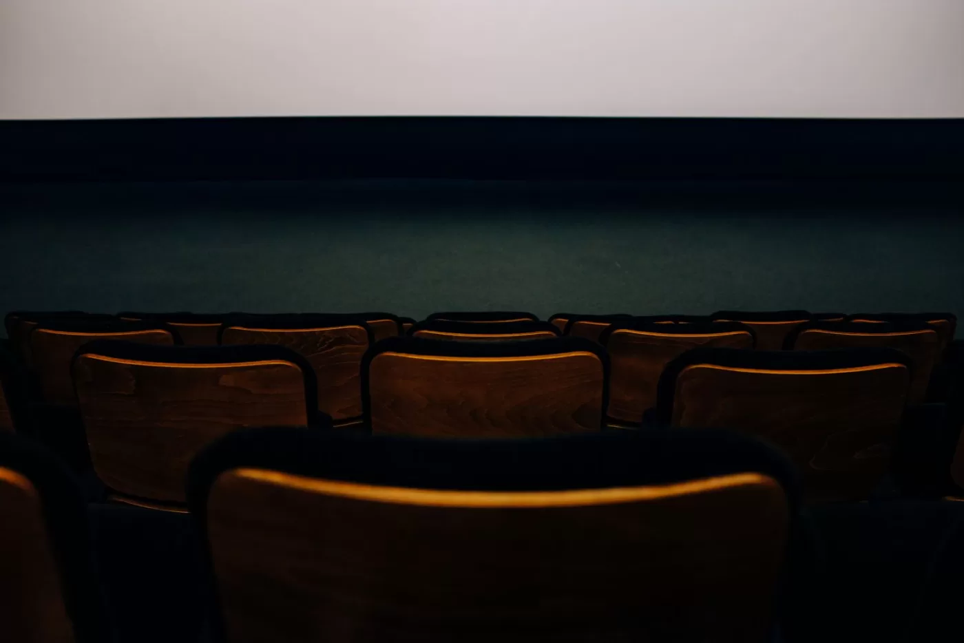 An empty auditorium with wooden seats facing a blank theater screen.