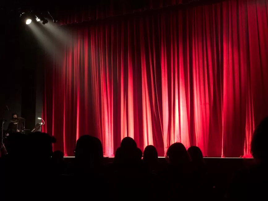 A red curtain and an audience in a darkened comedy room