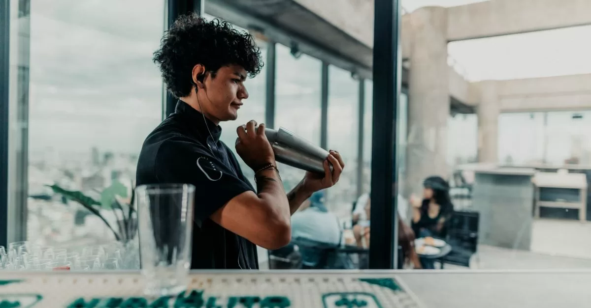 A bartender shaking a cocktail beside tall windows