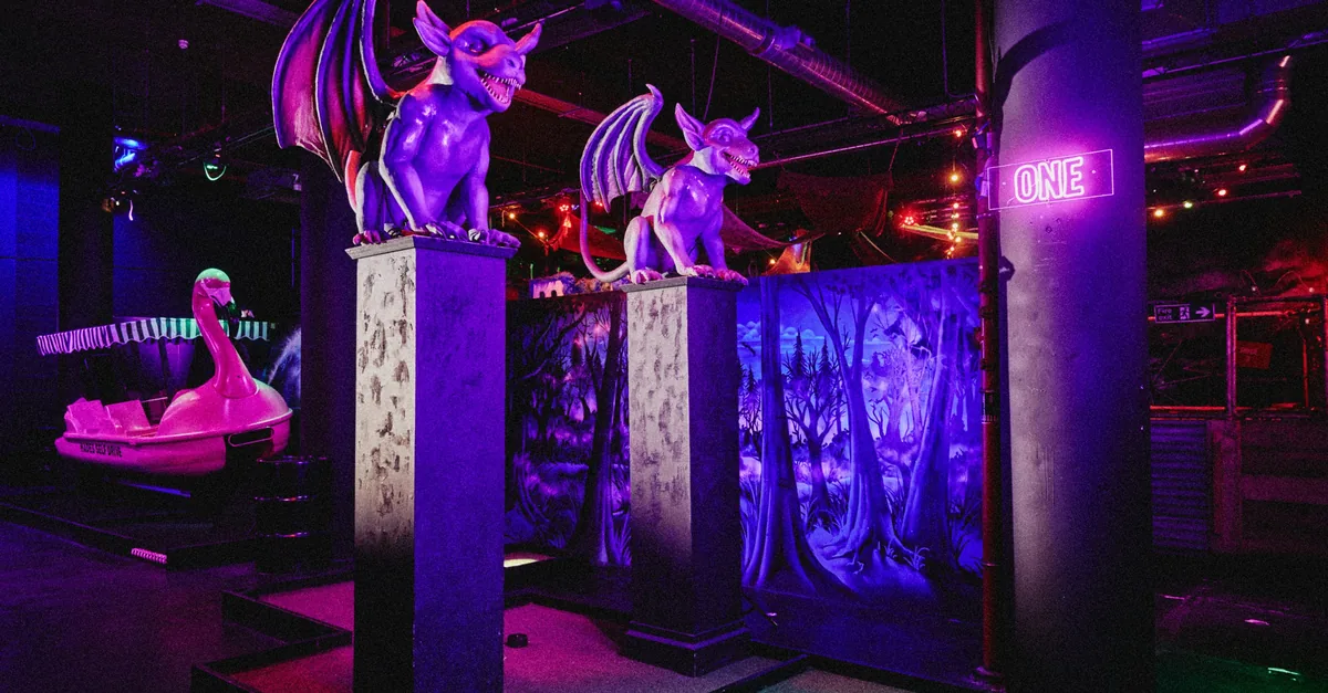 Two purple gargoyles on stone plinths under ultraviolet light beside a crazy golf hole