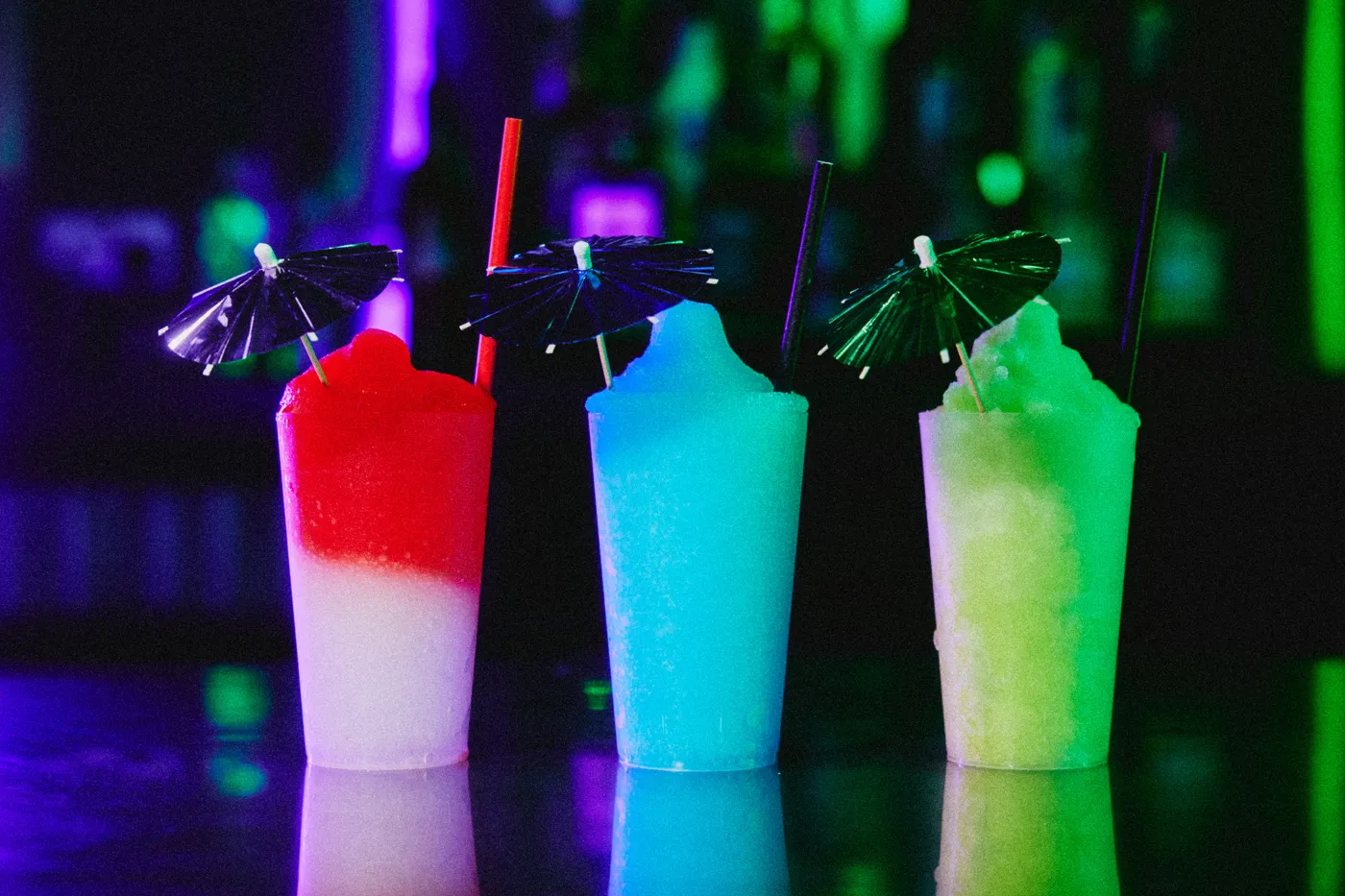 Three neon frozen drinks with paper umbrellas on a bar in the Oxford venue