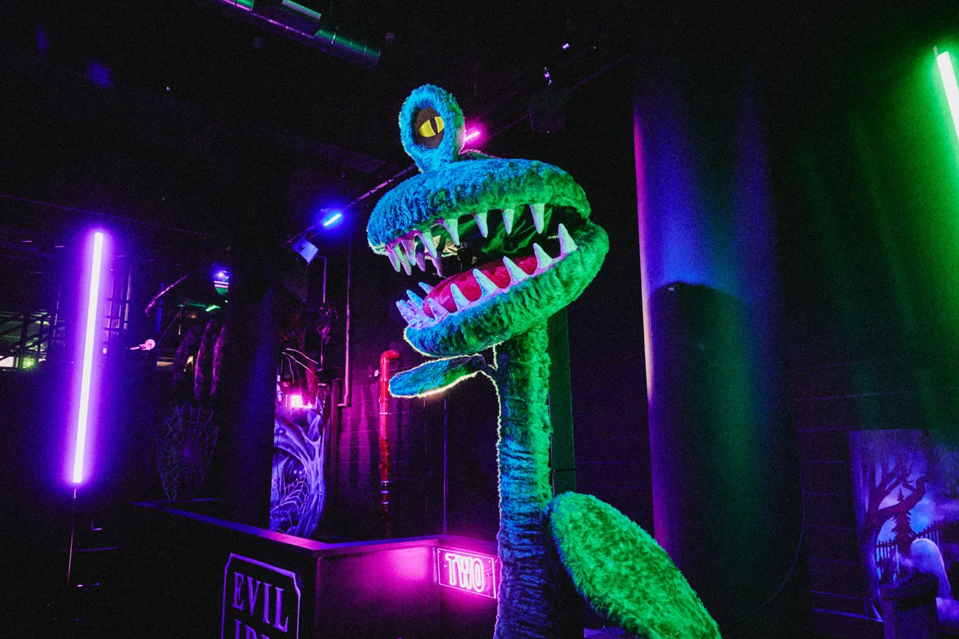 A giant furry green man-eating plant with teeth beside a neon sign reading TWO